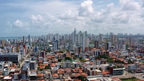 Toma-Aérea-De-Un-Camión-A-La-Derecha-De-La-Ciudad-De-Playa-Tropical-De-Cabedelo-Cerca-De-La-Ciudad-Capital-De-Joao-Pessoa,-Paraiba,-Brasil-Con-Grandes-Rascacielos-Y-Casas-Rurales-Debajo-En-Un-Cálido-Día-Soleado-De-Verano