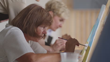 An-old-retired-woman-paints-a-picture-together-with-friends.-An-elderly-group-of-friends-and-a-senior-woman-are-drawing-pictures-together.