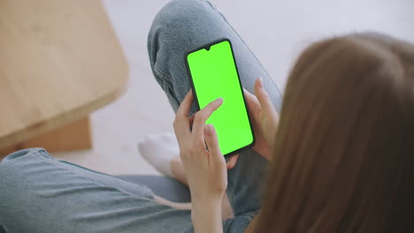 Point-of-View-of-Woman-at-Modern-Room-Sitting-on-a-Chair-Using-Phone-With-Green-Mock-up-Screen-Chroma-Key-Surfing-Internet-Watching-Content-Videos-Blogs-Tapping-on-Center-Screen