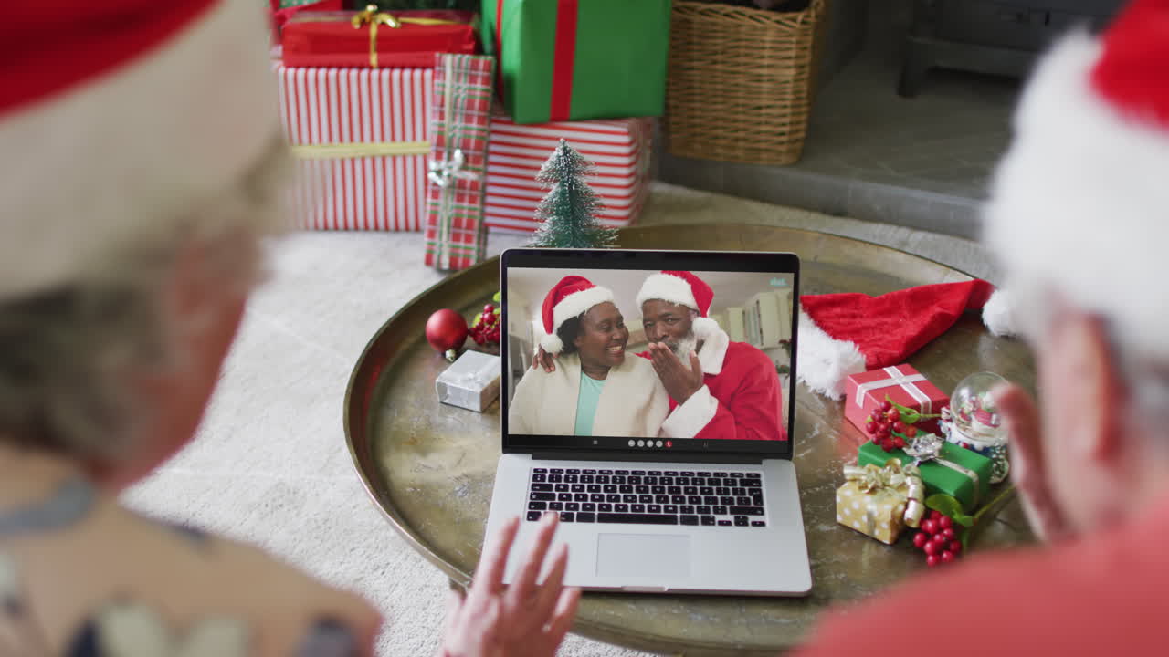 pareja caucásica de alto nivel con sombreros de santa usando una computadora portátil para una videollamada de navidad con pareja en la pantalla