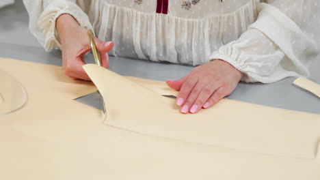 young female designer with tape-line on her neck standing in dressmaking studio and drawing lines with chalk and rule. female couturier in atelier cutting out a pattern for future clothes.