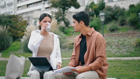 Young-colleagues-sitting-bench-vertically.-Positive-woman-taking-coffee-break