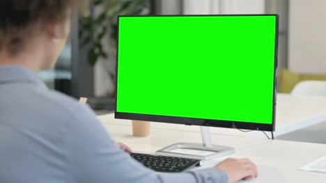 rear view of african woman using desktop with green chroma key screen