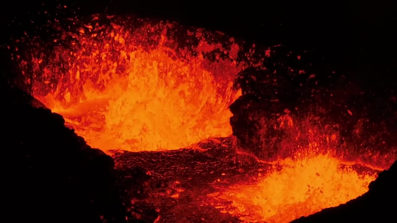 Riprese dall'alto di lava e magma incandescenti che schizzano drammaticamente in un cratere vulcanico attivo, mostrando la potenza primordiale della natura e i colori vividi della roccia fusa contro le scure pareti del cratere in Islanda