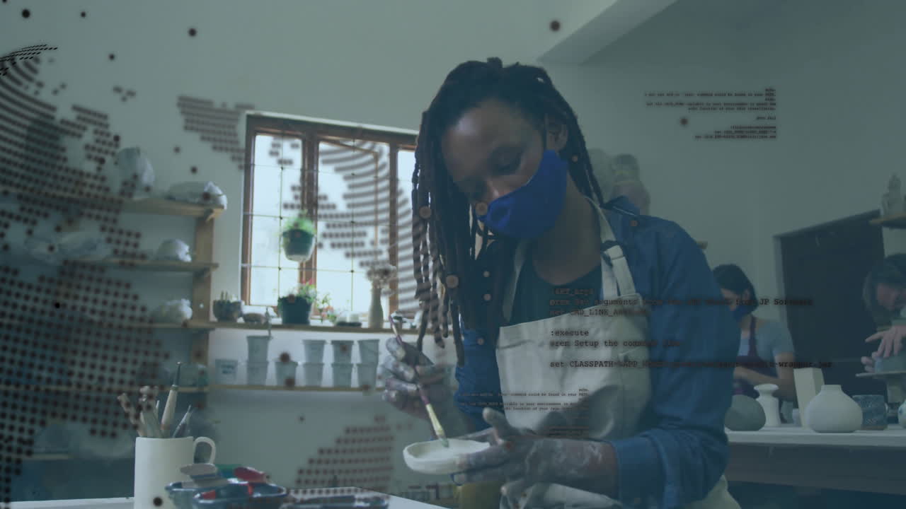 Painting pottery in studio, artist wearing mask with animation digital data overlay