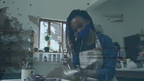 painting pottery in studio, artist wearing mask with animation digital data overlay