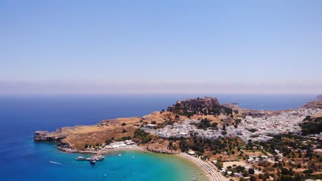 aerial view of lindos beach, white houses of village and acropolis in background, rhodes, greece - drone shot