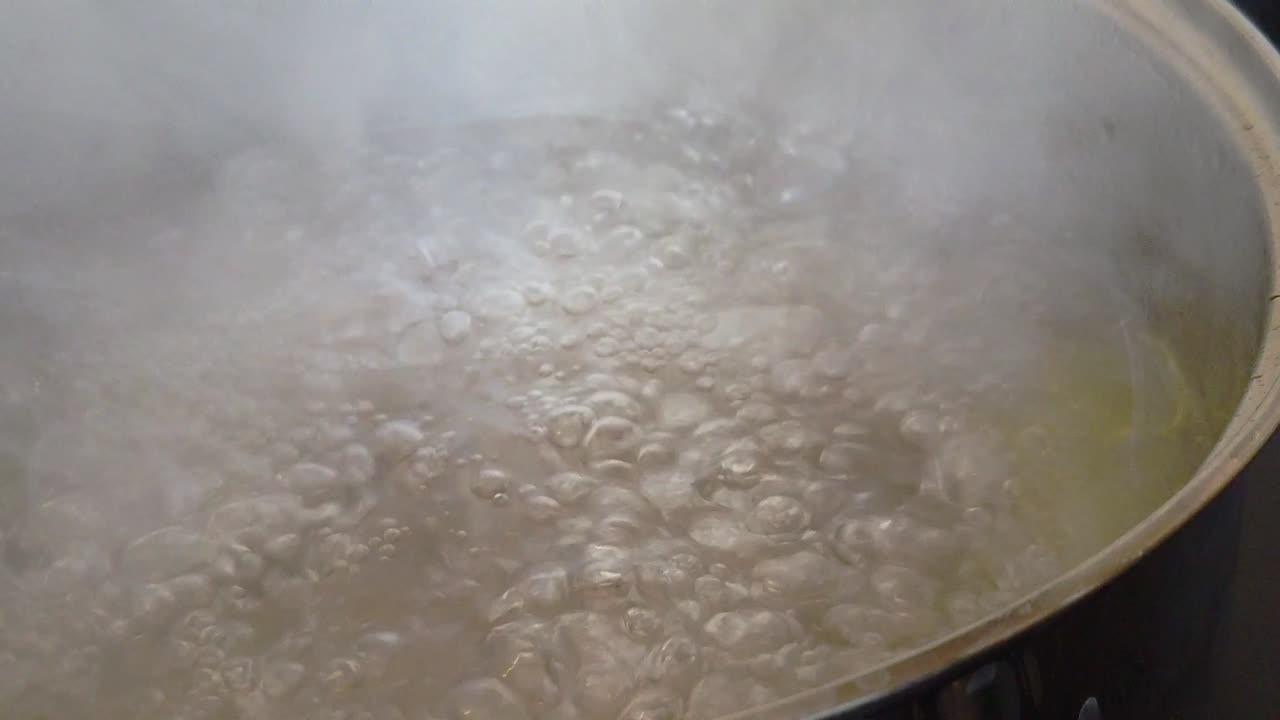 Slow motion clip of a stainless steel saucepan of water and olive oil at a rolling boil.