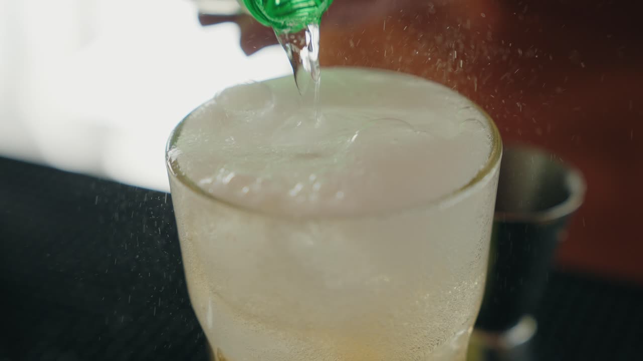 Close up fizzy beverage being poured into cold glass with ice cubes indoors