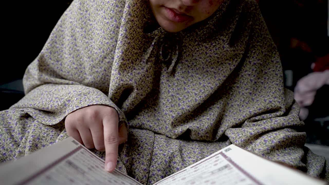 niño con ropa tradicional absorto en la lectura del corán, en el interior, íntimo primer plano