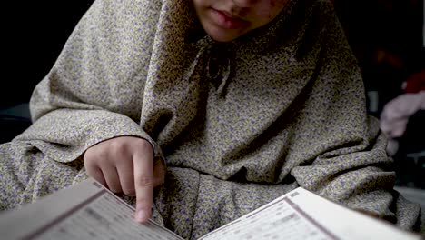 niño con ropa tradicional absorto en la lectura del corán, en el interior, íntimo primer plano