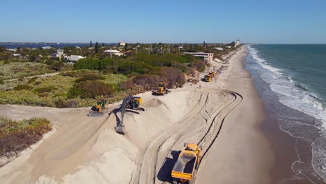 4k drone shot of excavators driving on the beach near the ocean water