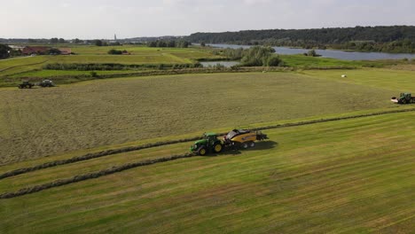 un trattore verde con rimorchio giallo produce balle di fieno in un paesaggio panoramico