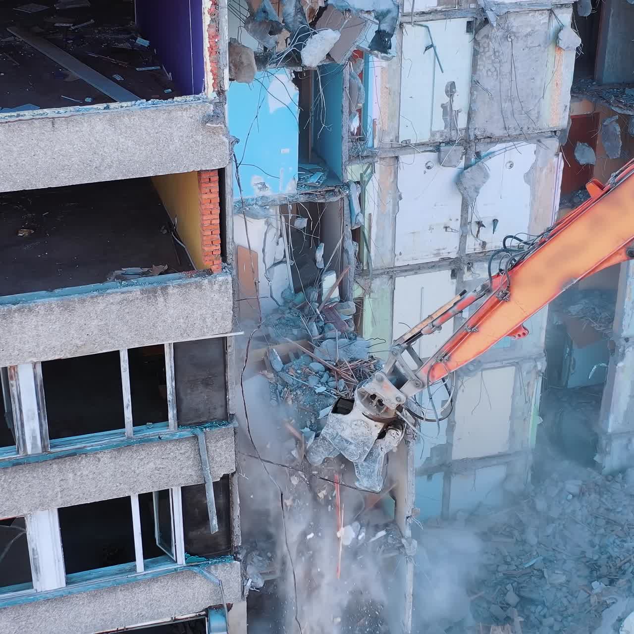 Demolition machine is breaking the floors into pieces and throwing them down. Powerful claw of excavator demolishing the ruined building