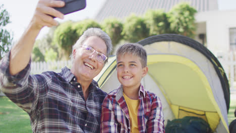 happy caucasian grandfather and grandson sitting in tent and taking selfie, slow motion