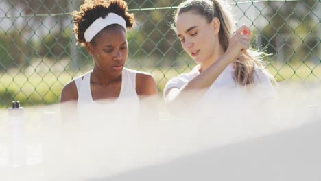 Video-of-happy-diverse-female-tennis-players-sitting,-talking-and-resting-after-match