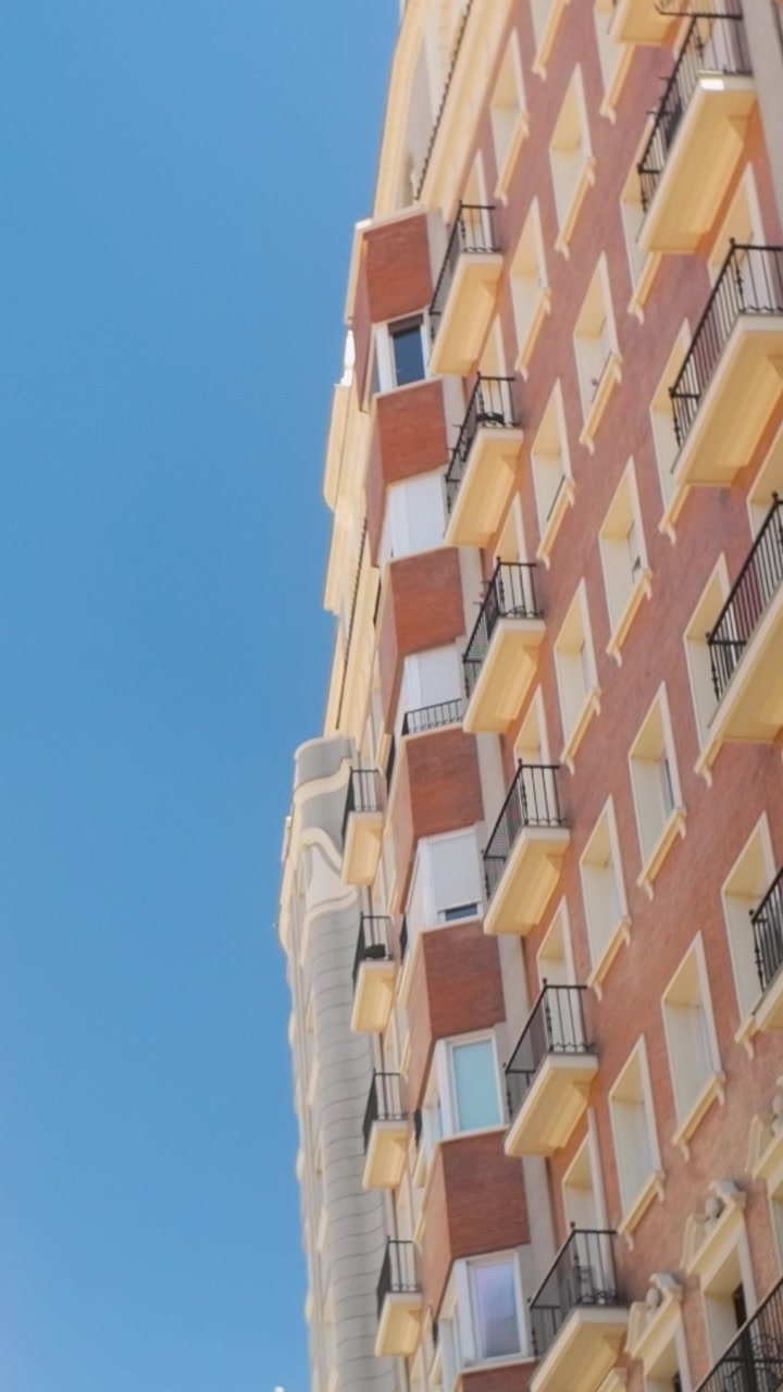 Uma fotografia vertical de baixo ângulo de uma fachada clássica de edifício de apartamentos espanhol com varandas contra um céu azul claro em Madrid
