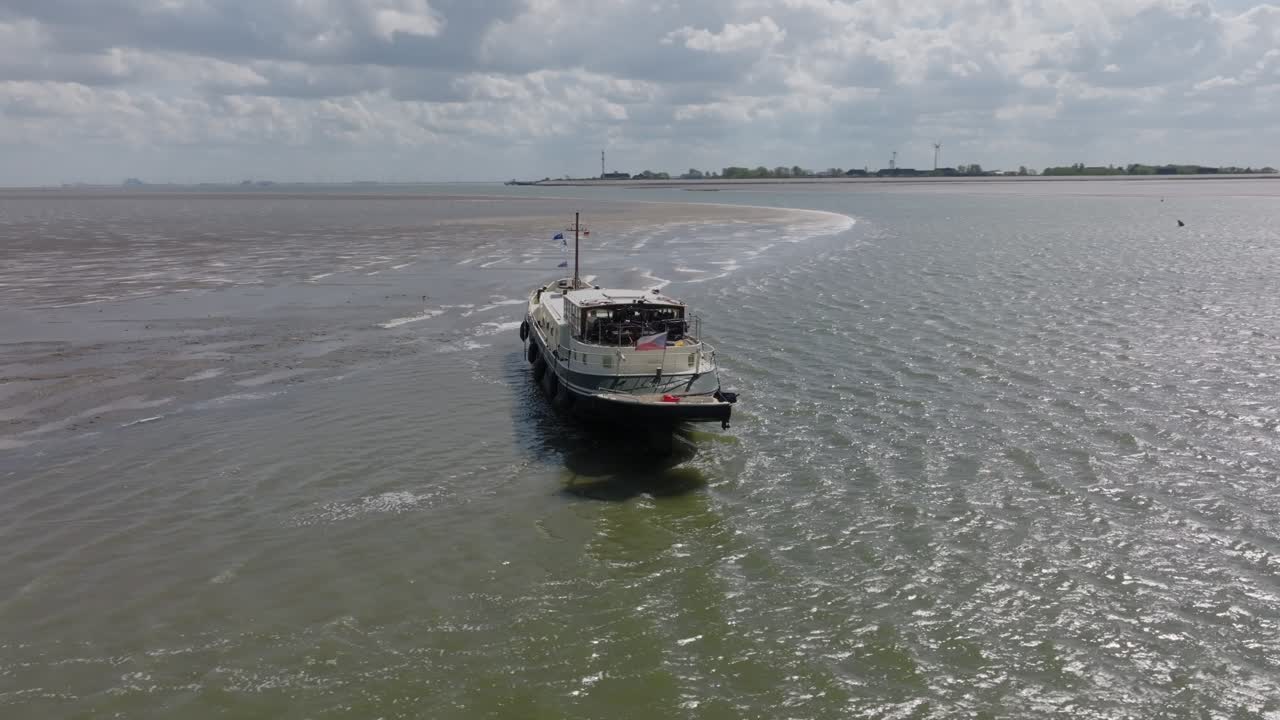 Traditional vessel grounded on shallow tidal flats at low tide; stern three‑quarter perspective in daylight