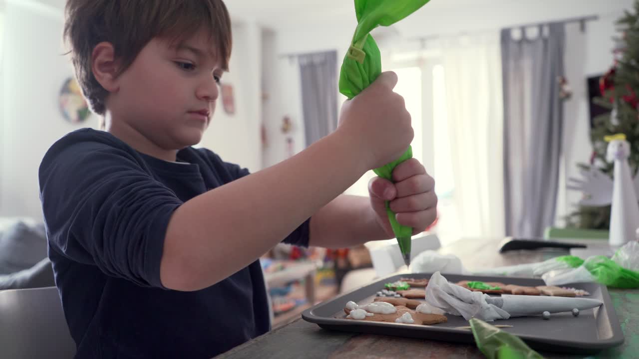 Un bambino caucasico decora biscotti di pan di zenzero natalizi a casa, usando una sac à poche.