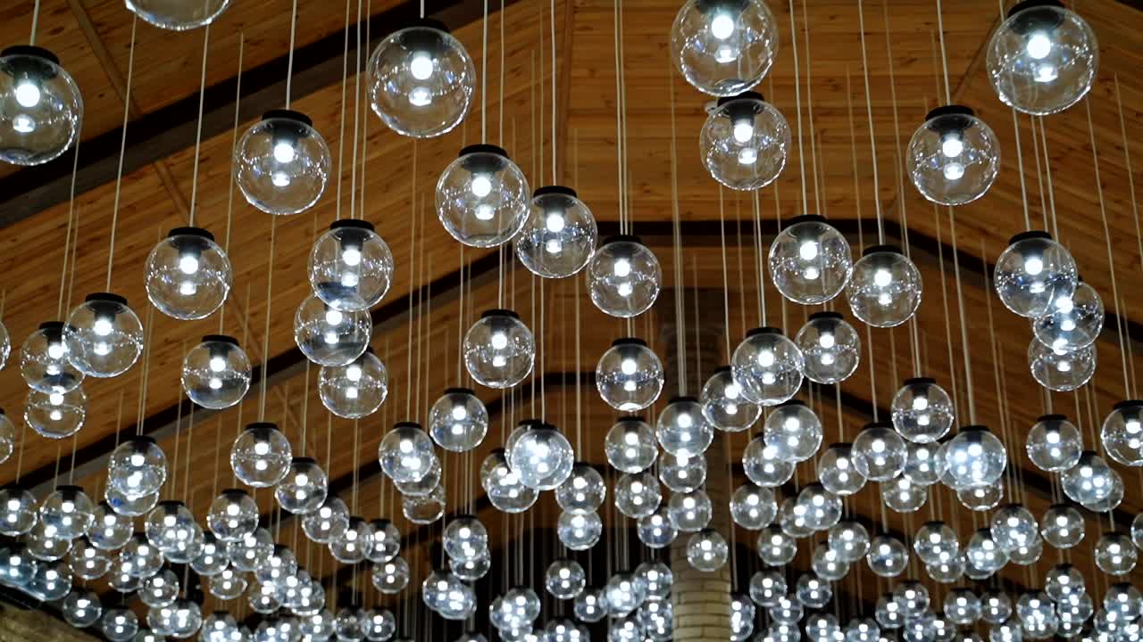 Many round light bulbs background. Beautiful ceiling with shining glass balls hanging on long white wires. Glamour ceiling.