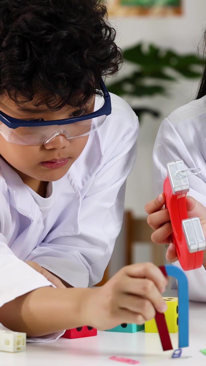 Siswa yang fokus mengenakan kacamata pengaman menggunakan magnet tapal kuda selama kegiatan STEM di kelas sekolah dasar