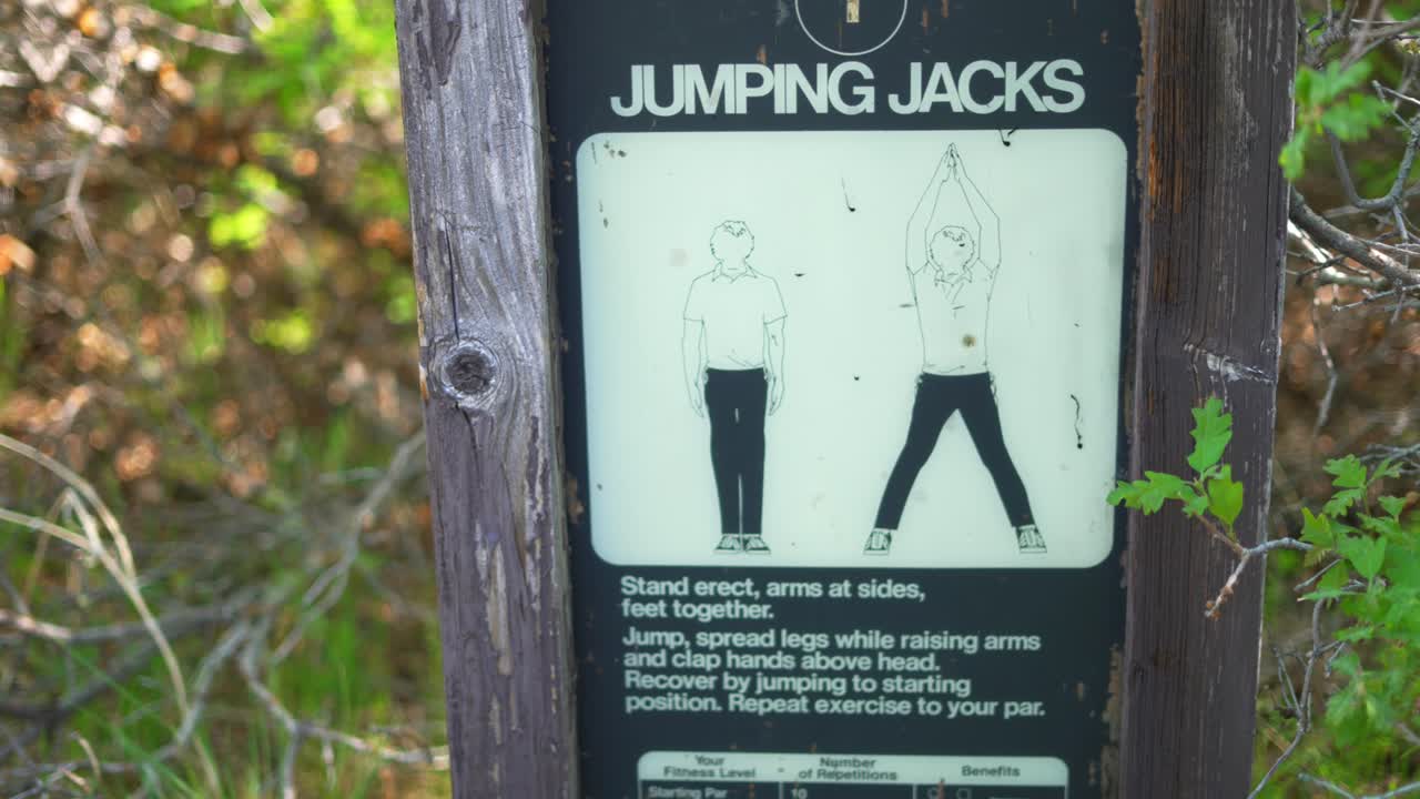 Old worm jumping jacks instruction demo sign posted on wood frame a long time ago outside at workout fitness hiking trail public national park