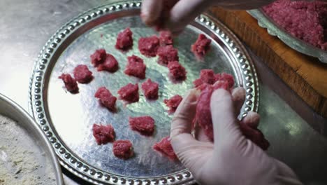 the chef cuts the minced meat into small pieces with her hands and puts it on the tray