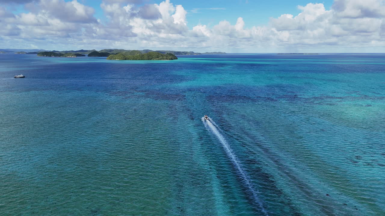 High-quality drone shot gliding around the glowing waters and emerald island dots surrounding Palau. Revealing drone shot of boat in the water