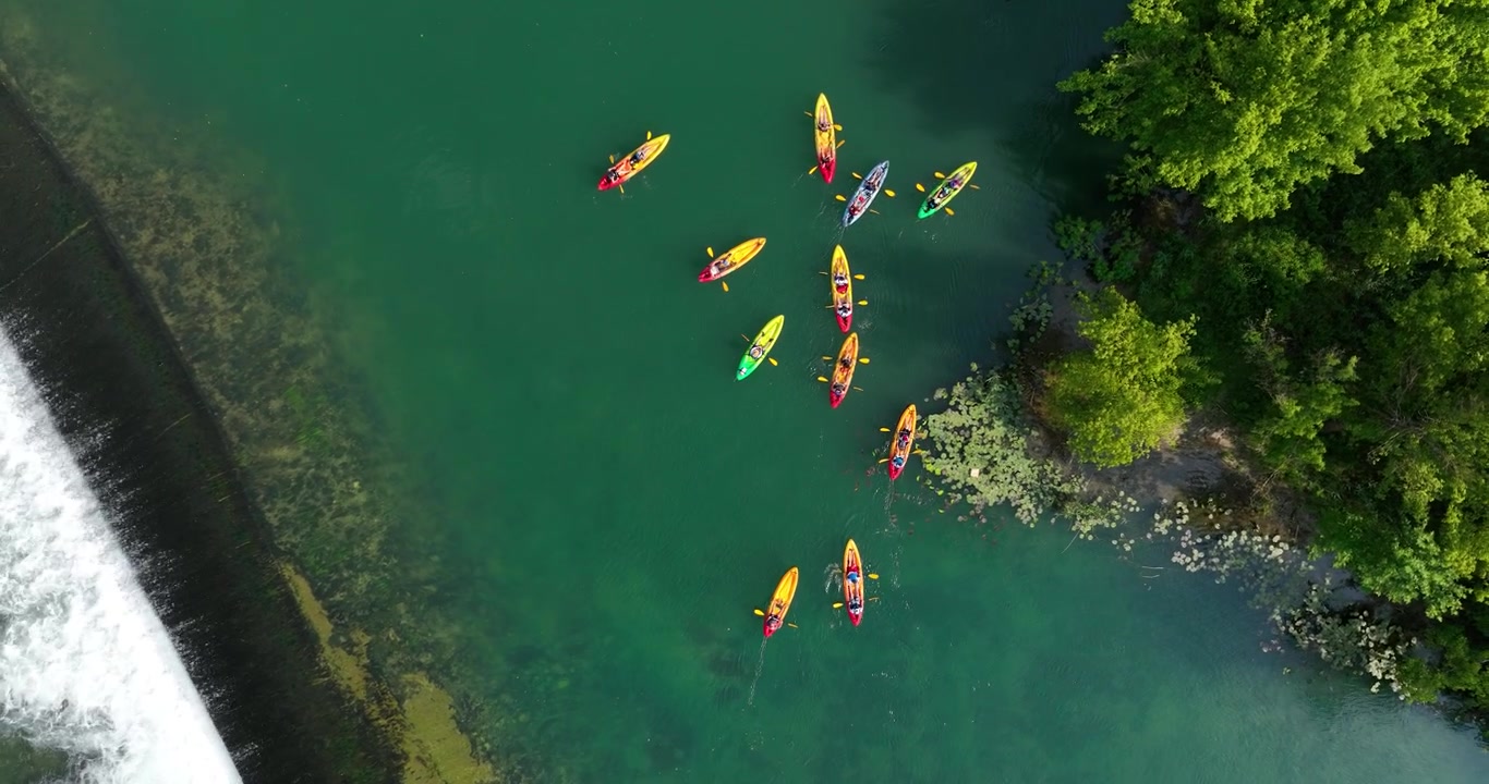 Vista aérea de un grupo de personas haciendo kayak en un río con árboles verdes cerca.
