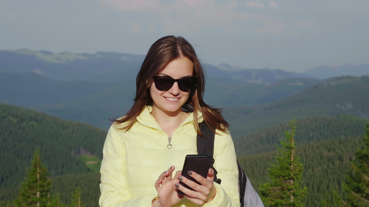 mujer joven disfrutando de un teléfono inteligente en un pintoresco telón de fondo de montañas cubiertas de bosque siempre