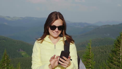 Young-Woman-Enjoying-A-Smartphone-On-A-Picturesque-Backdrop-Of-Mountains-Covered-With-Forest-Always-