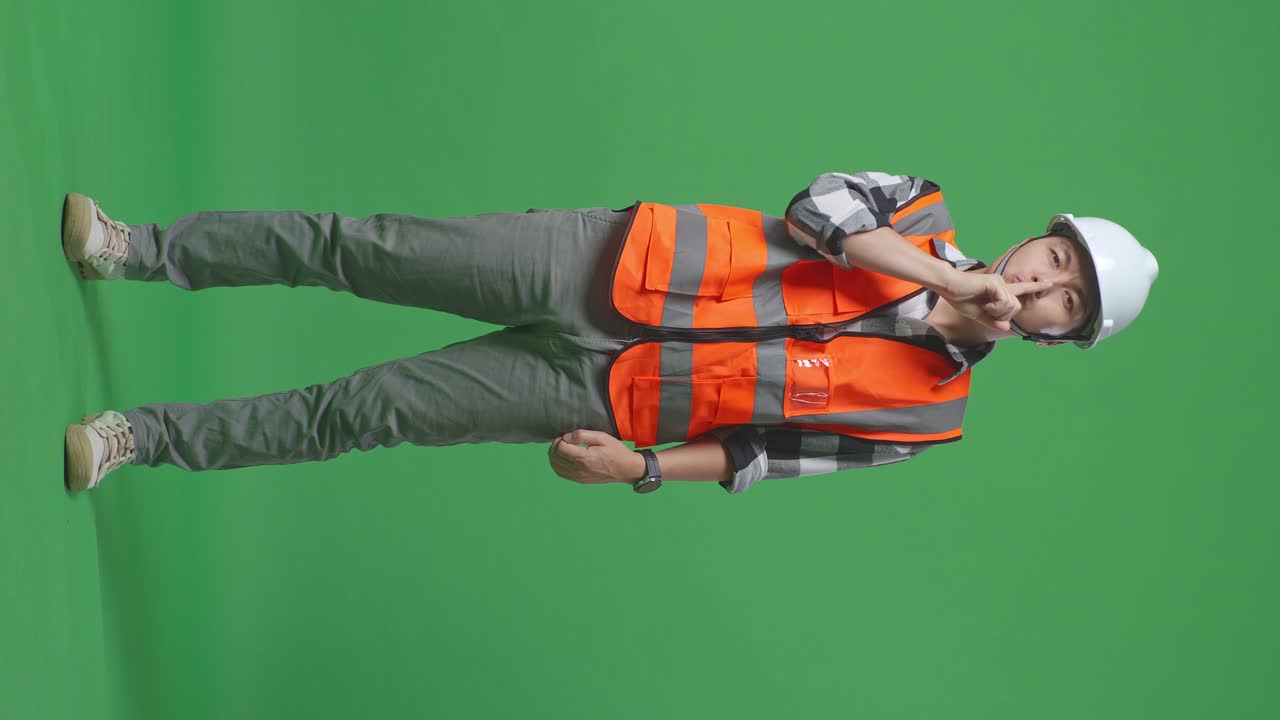 Full Body Of Asian Male Engineer With Safety Helmet Making Shh Gesture While Standing In The Green Screen Background Studio
