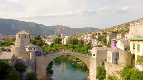 drone ascend over neretva river with people walking at stari most, old bridge in mostar, bosnia and herzegovina