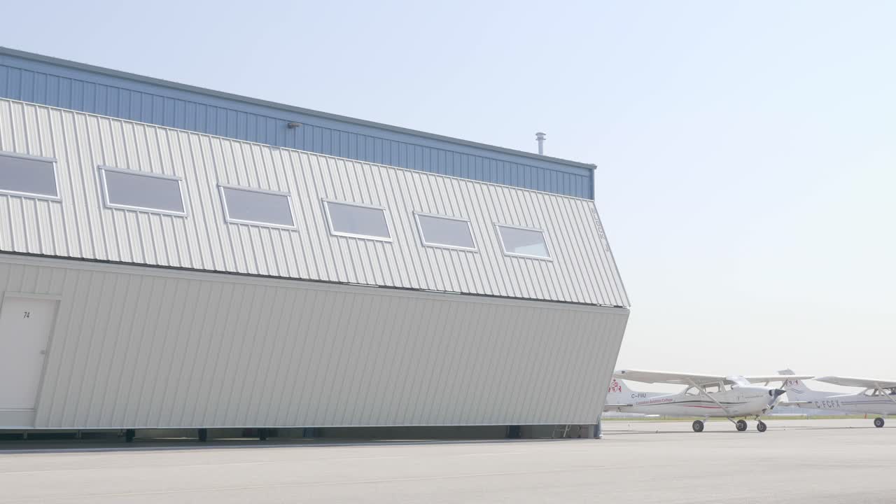 las puertas del hangar del aeródromo se abren revelando un avión bimotor estacionado