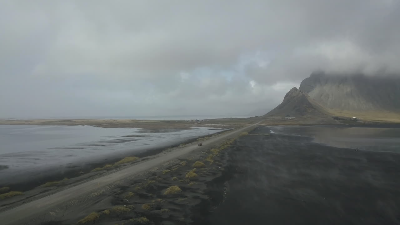 camino de grava con la montaña vestrahorn y un auto conduciendo en un día brumoso en islandia - toma aérea de drones