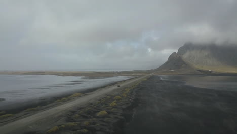 Schotterstraße-Mit-Dem-Berg-Vestrahorn-Und-Einem-Auto,-Das-An-Einem-Nebligen-Tag-In-Island-Fährt---Luftdrohnenaufnahme