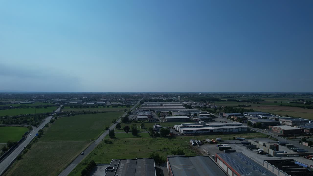 Vista aerea con drone ad alta quota sulla zona industriale nella Pianura Padana che mostra fabbriche, magazzini, strade e terreni agricoli circostanti, a illustrare lo sviluppo industriale integrato in un'area rurale