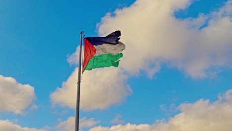 old and ruined palestine national flag waving against blue cloudy sky