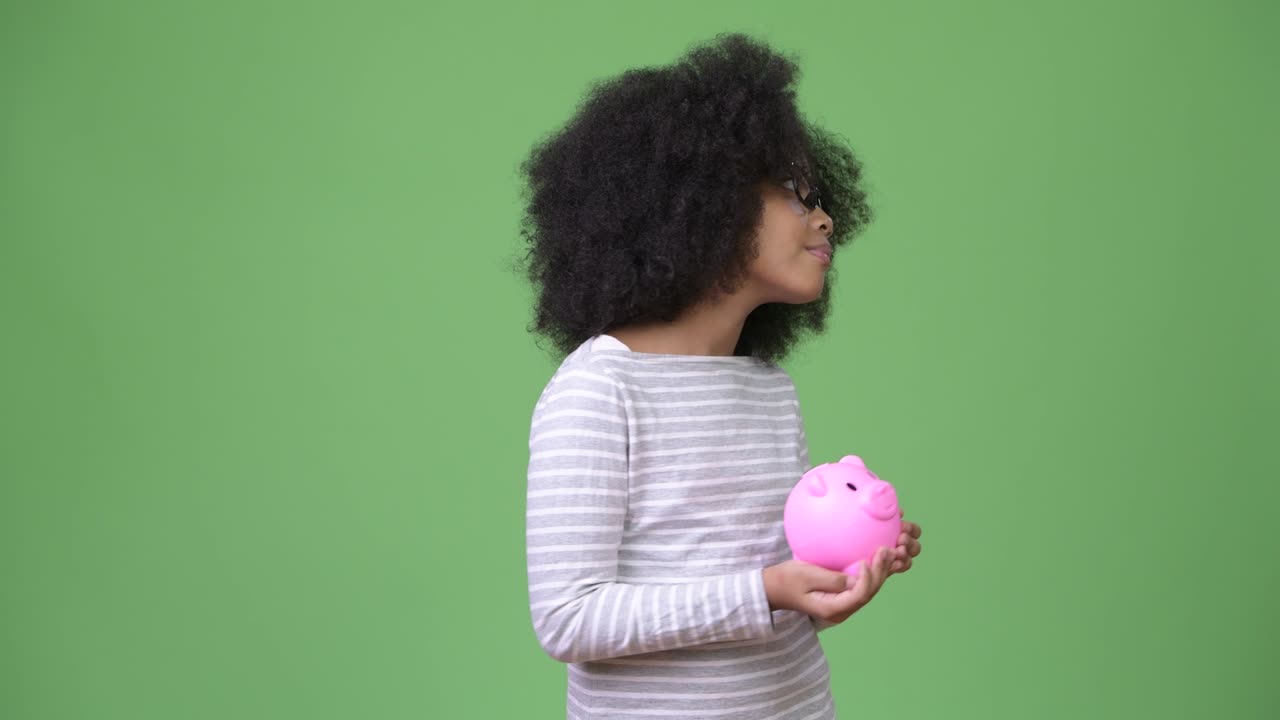 Jovem e fofa garota africana com cabelo afro segurando um cofrinho.