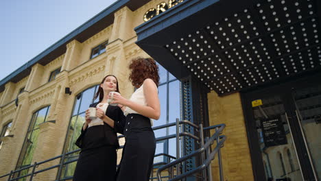 Business-women-talking-near-office.-Smiling-ladies-standing-with-cups-outdoors.