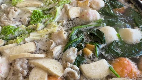 a bubbling hotpot filled with vegetables, meat, and fish balls in a rich broth. vibrant colors and steaming atmosphere