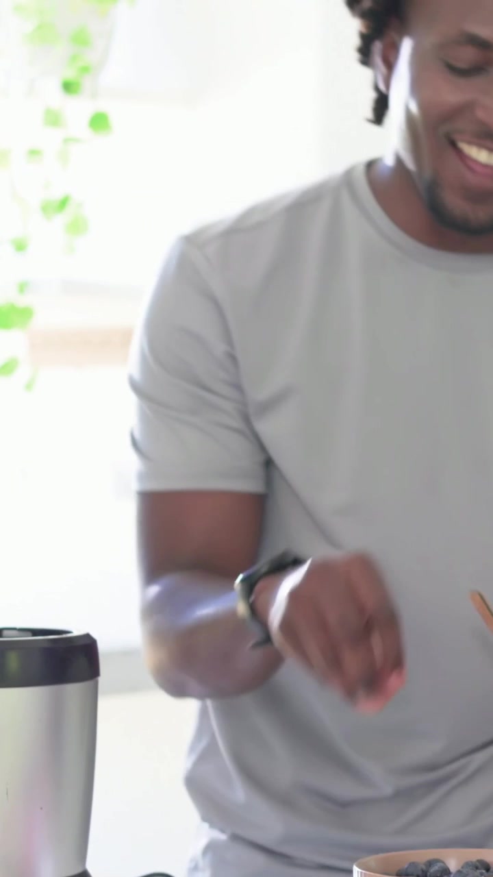 Vertical video: Reaching bowls, man gray T watch picking berries to blender in kitchen, copy space