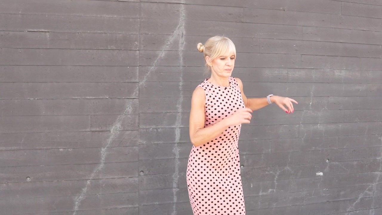 Una donna balla indossando un vestito a pois con un muro di mattoni urbano sullo sfondo.