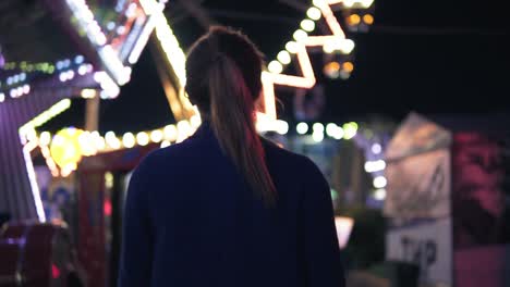 Back-view-of-young-attractive-girl-walking-forward-then-turning-around-smiling-and-looking-at-camera-hanging-out-in-amusement