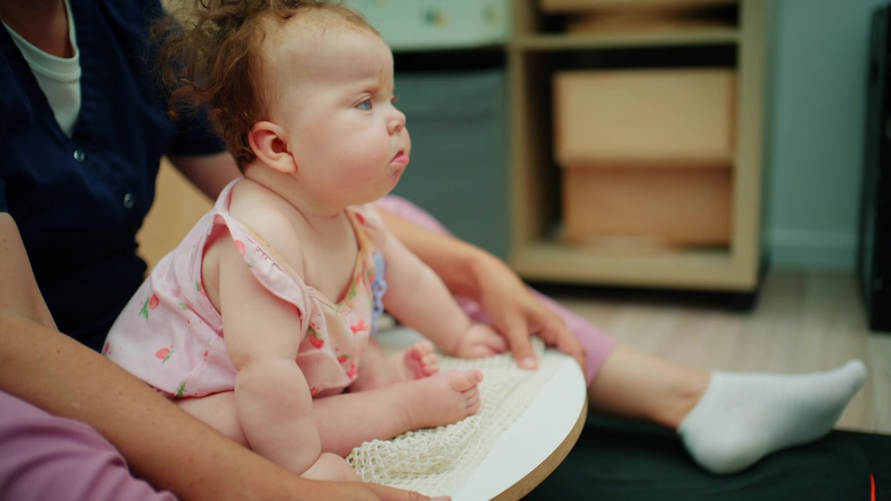 Baby with down syndrome training motor skills during a physical therapy session with a specialist in a home environment