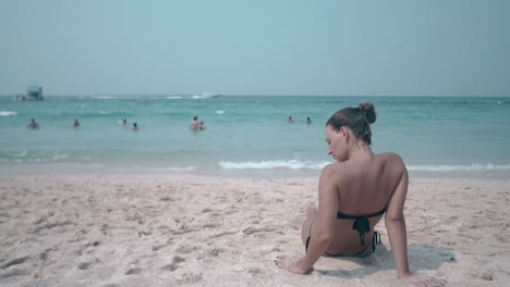 una chica delgada yace en una playa de arena amarilla contra el océano azul
