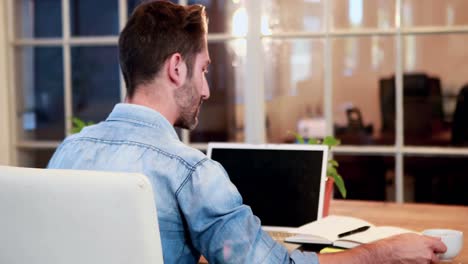 hombre de negocios casual bebiendo una bebida caliente frente a una computadora portátil