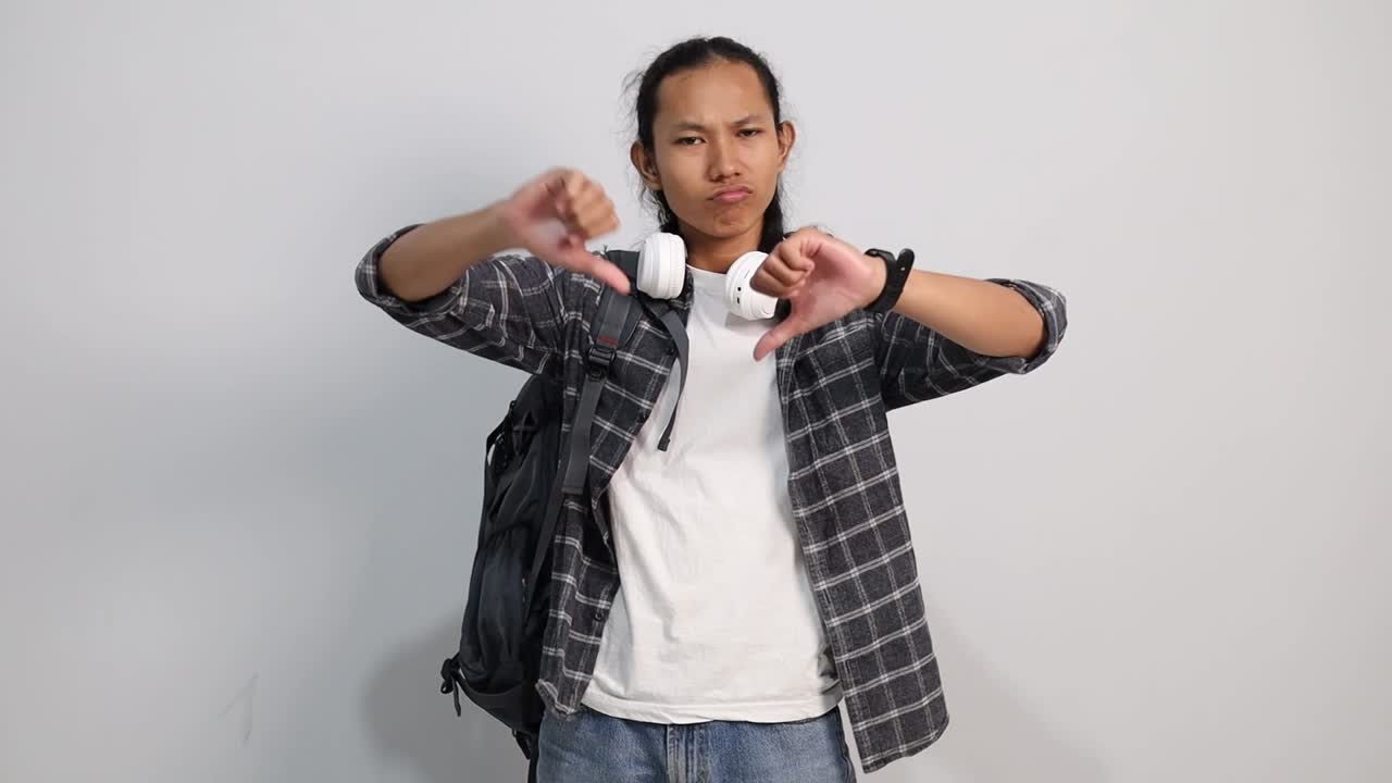 Unhappy Young Asian college student showing thumbs down and expressing dislike