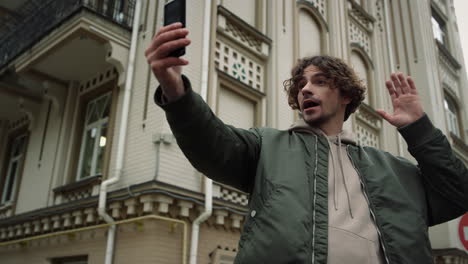 young man using phone for video call outdoor. guy waving hand to camera in city.