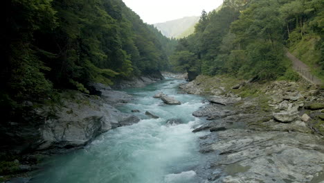 backwards tracking aerial over blue-green river flowing through mountains on the island of shikoku, japan